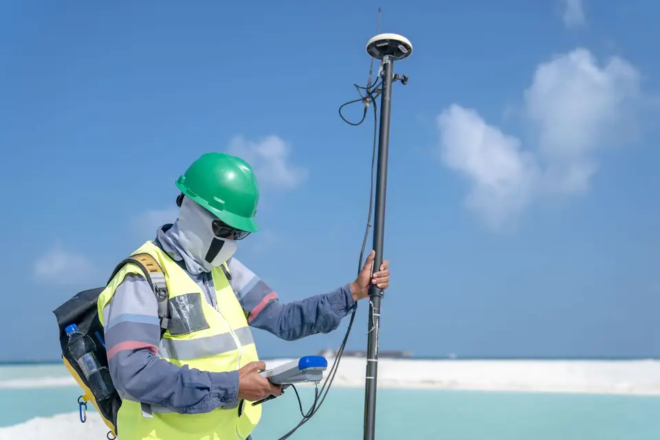 Topógrafo con receptor GNSS sobre jalón junto al mar